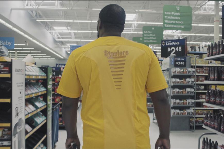 Ein muskulöser Mann geht durch die Reihen eines Supermarkts.