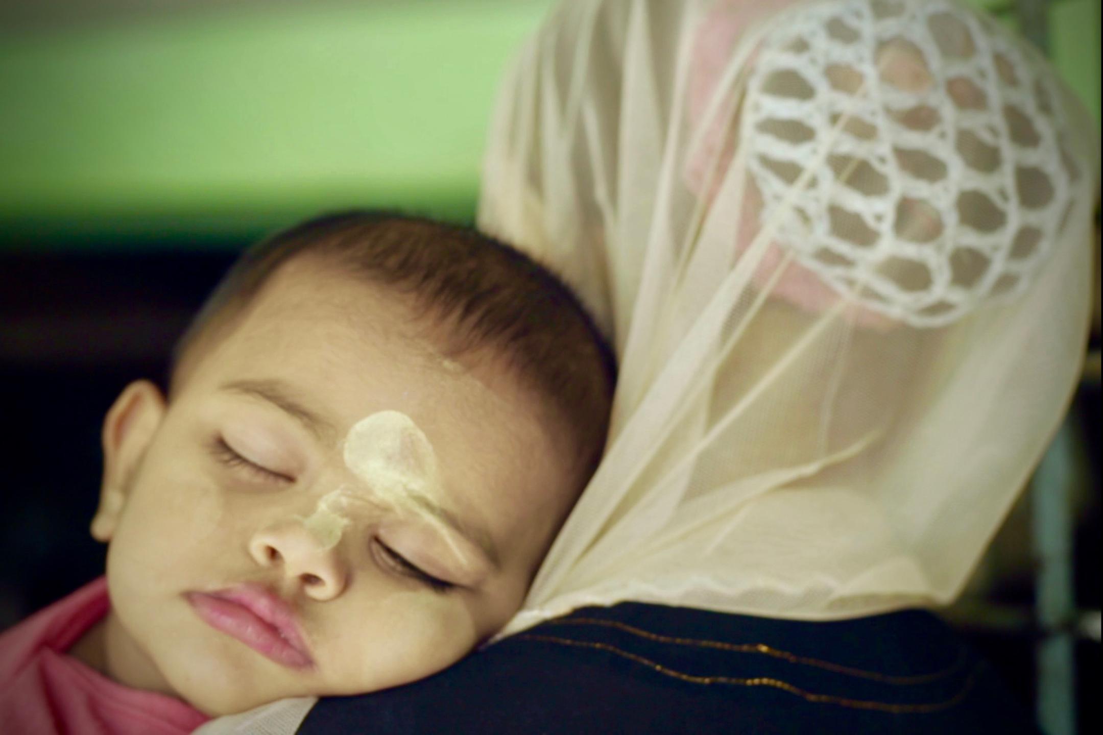 A baby is sleeping with its head resting on the shoulder of its mother.