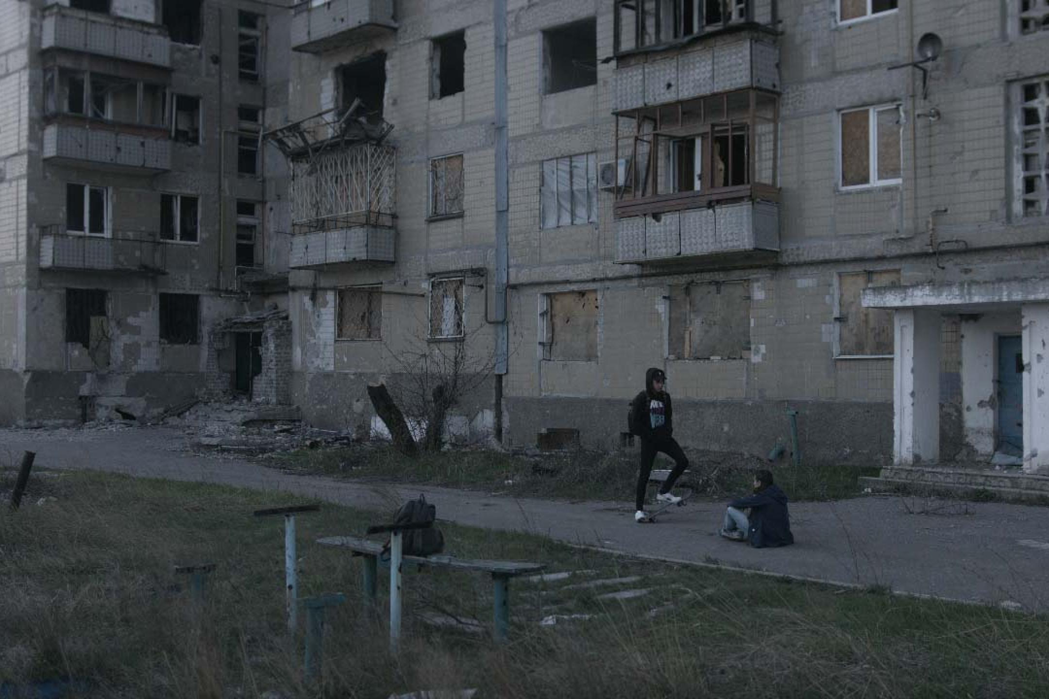 Eine Aufnahme in der Dämmerung: Zwei Jugendliche hängen vor einem leer stehenden, heruntergekommenem Wohnblock rum. 