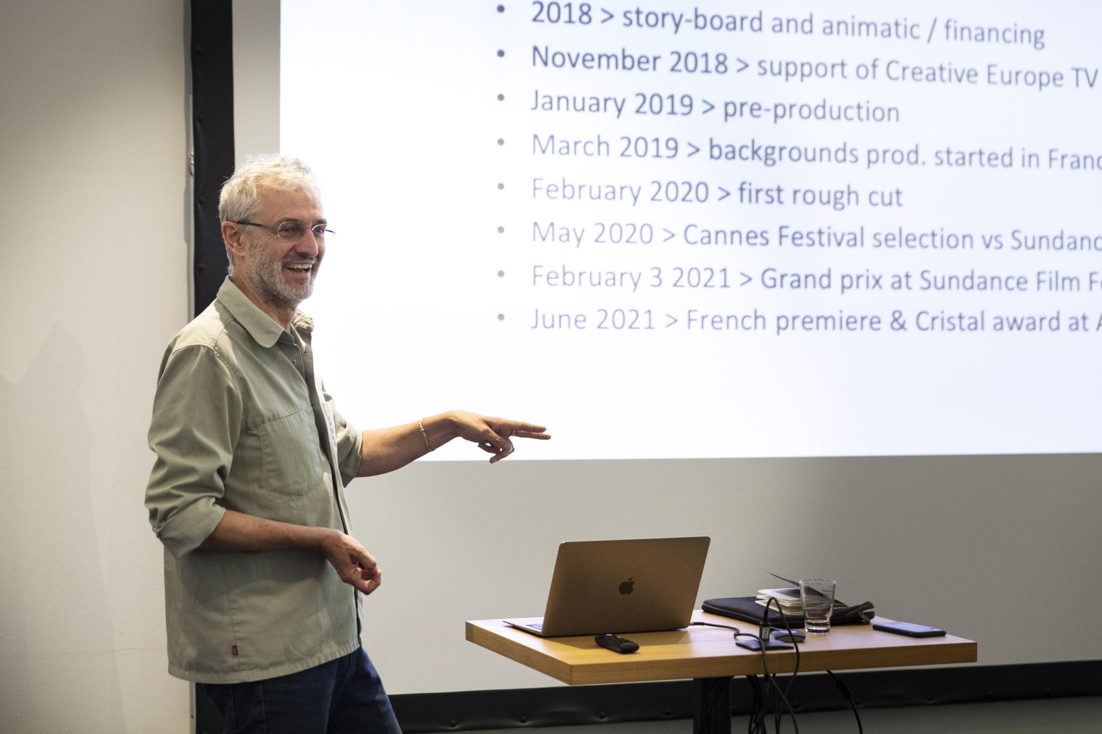 A man stands in front of a huge screen with a timeline on it. He smiles widely.