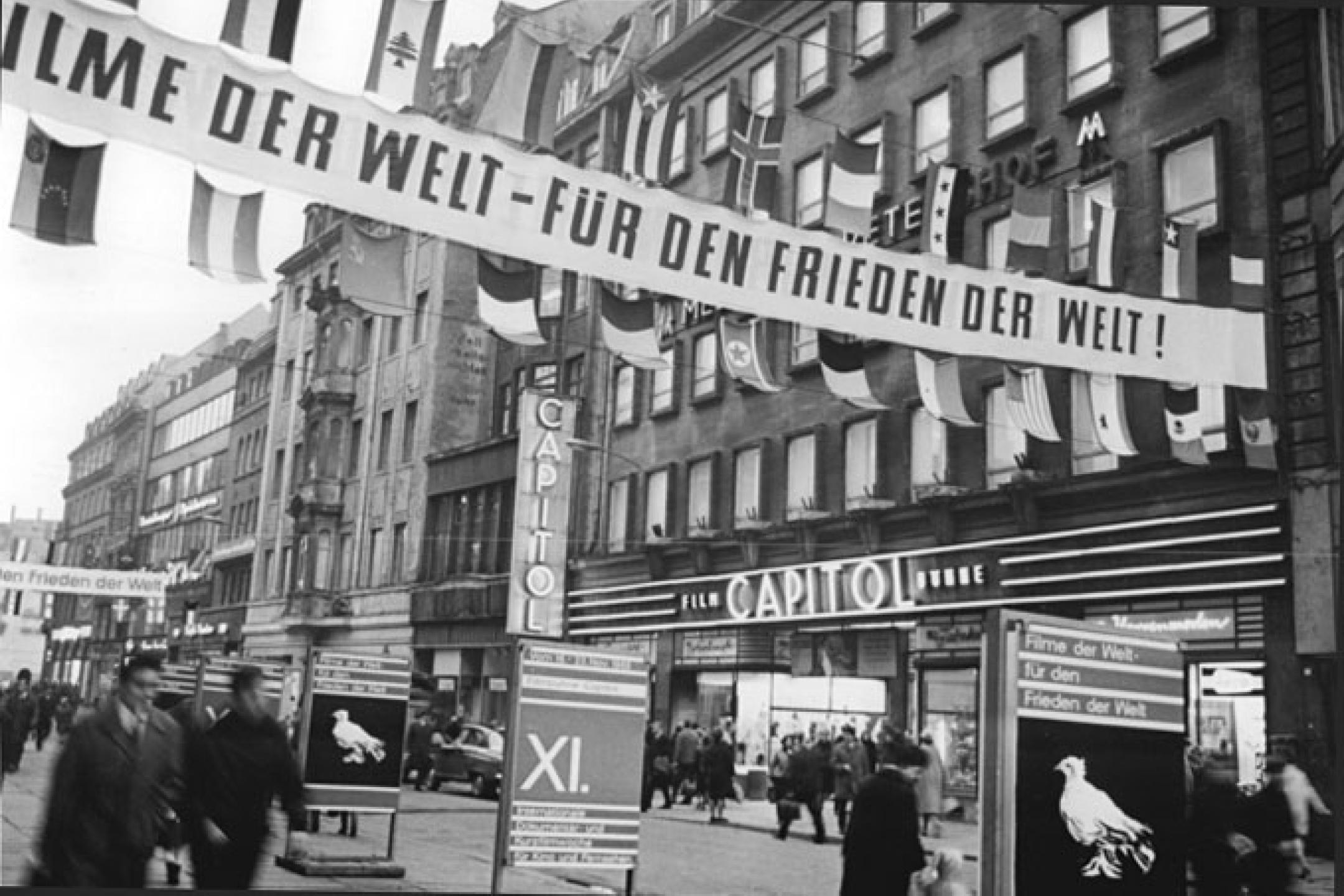 Die Petersstraße in Leipzig. Über der Straße hängt ein Banner mit dem Text "Filme der Welt für den Frieden der Welt".