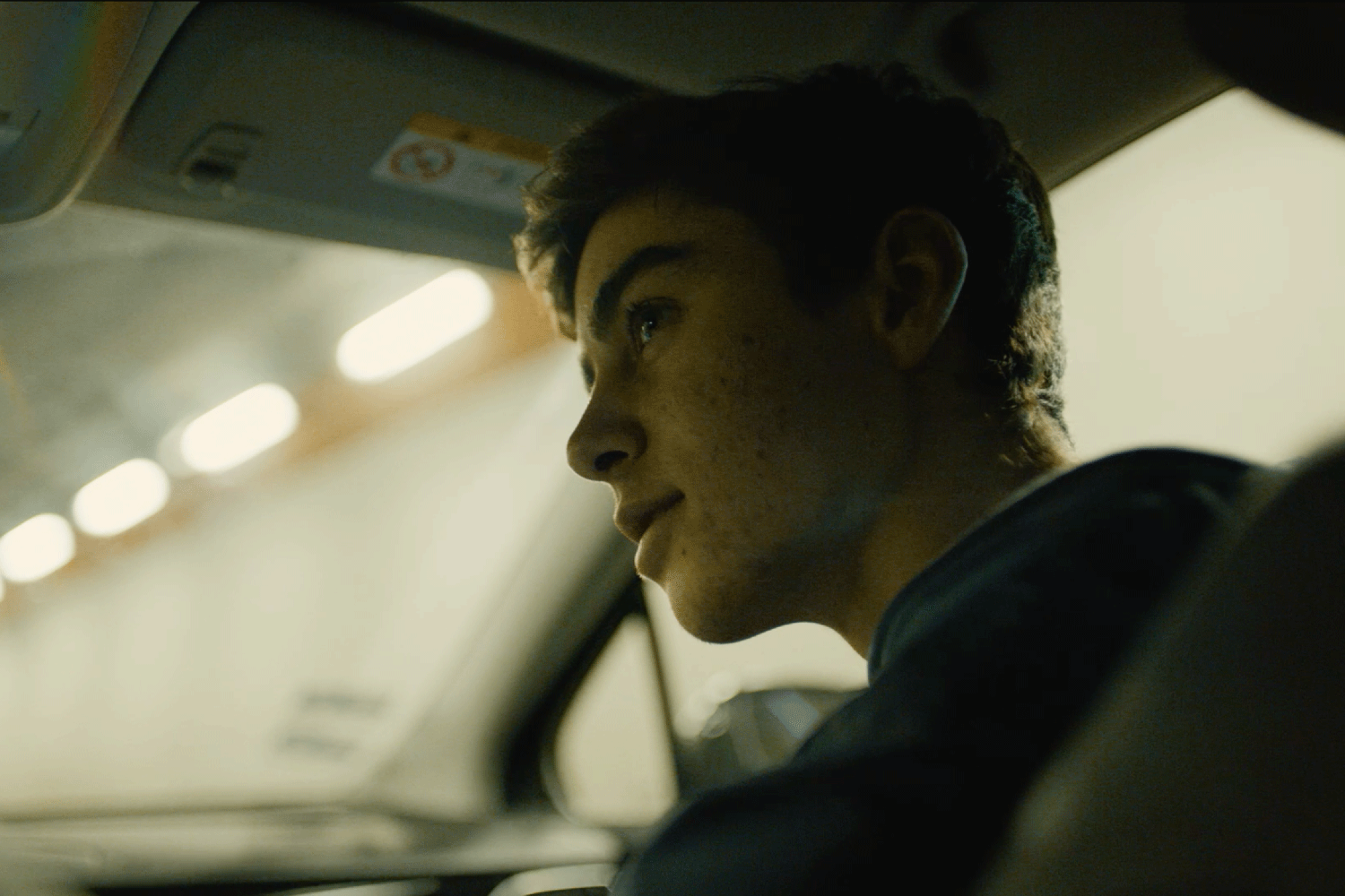 A young men sits in the front passenger seat in a car.