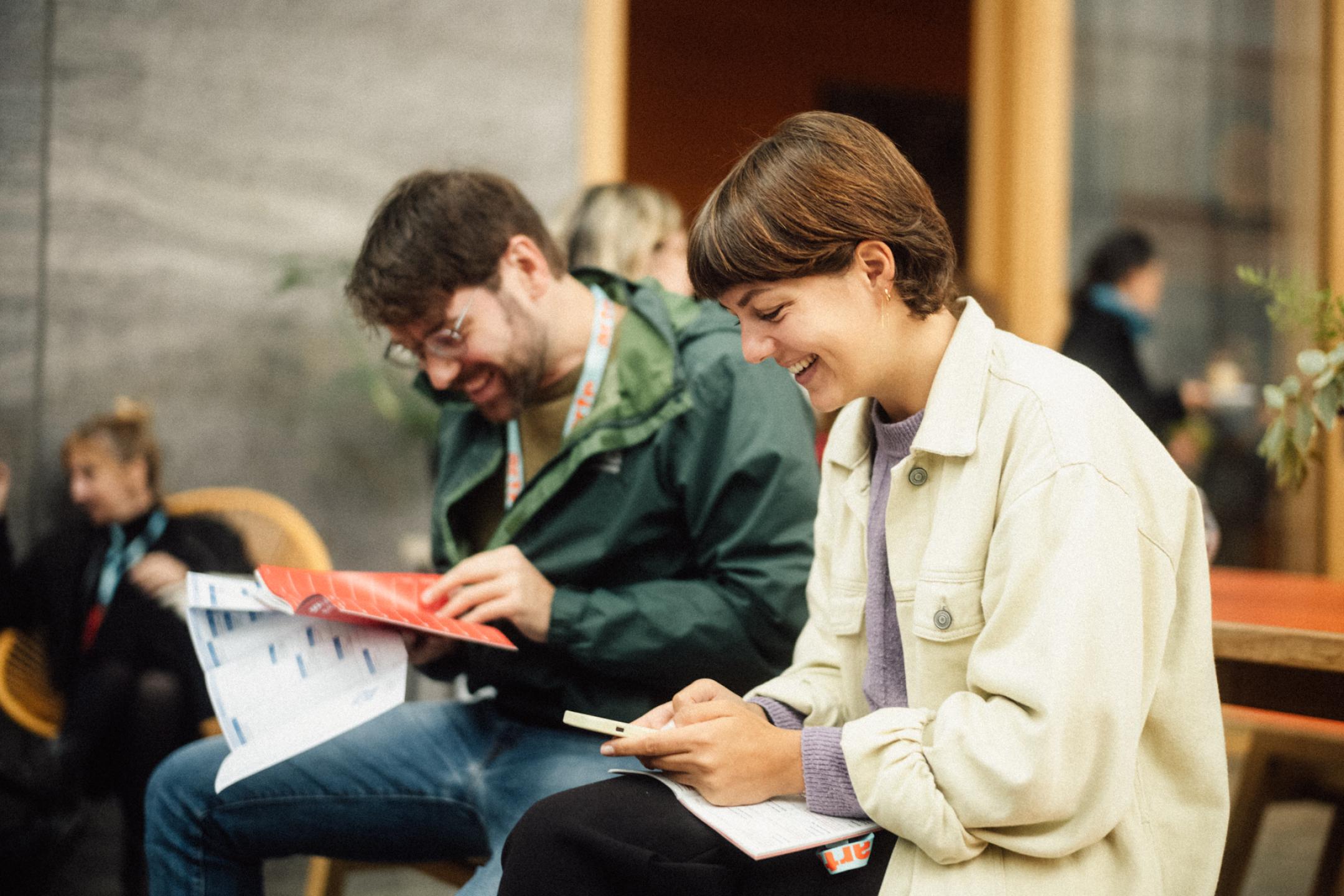 Zwei Personen sitzen auf nebeneinander und blättern im Festivalprogramm.