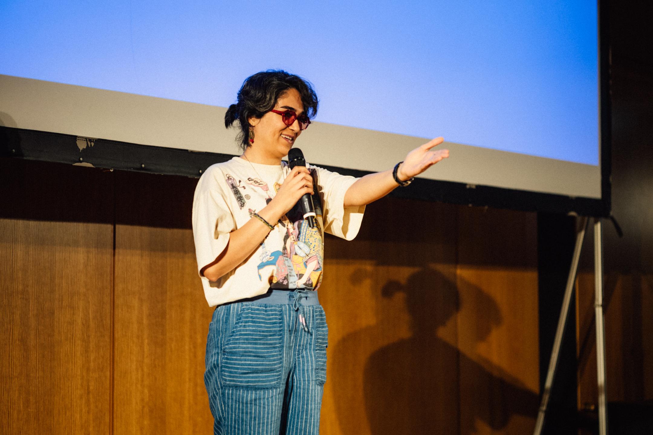 A woman speaking into a microphone is extending her hand to point to someone in the audience