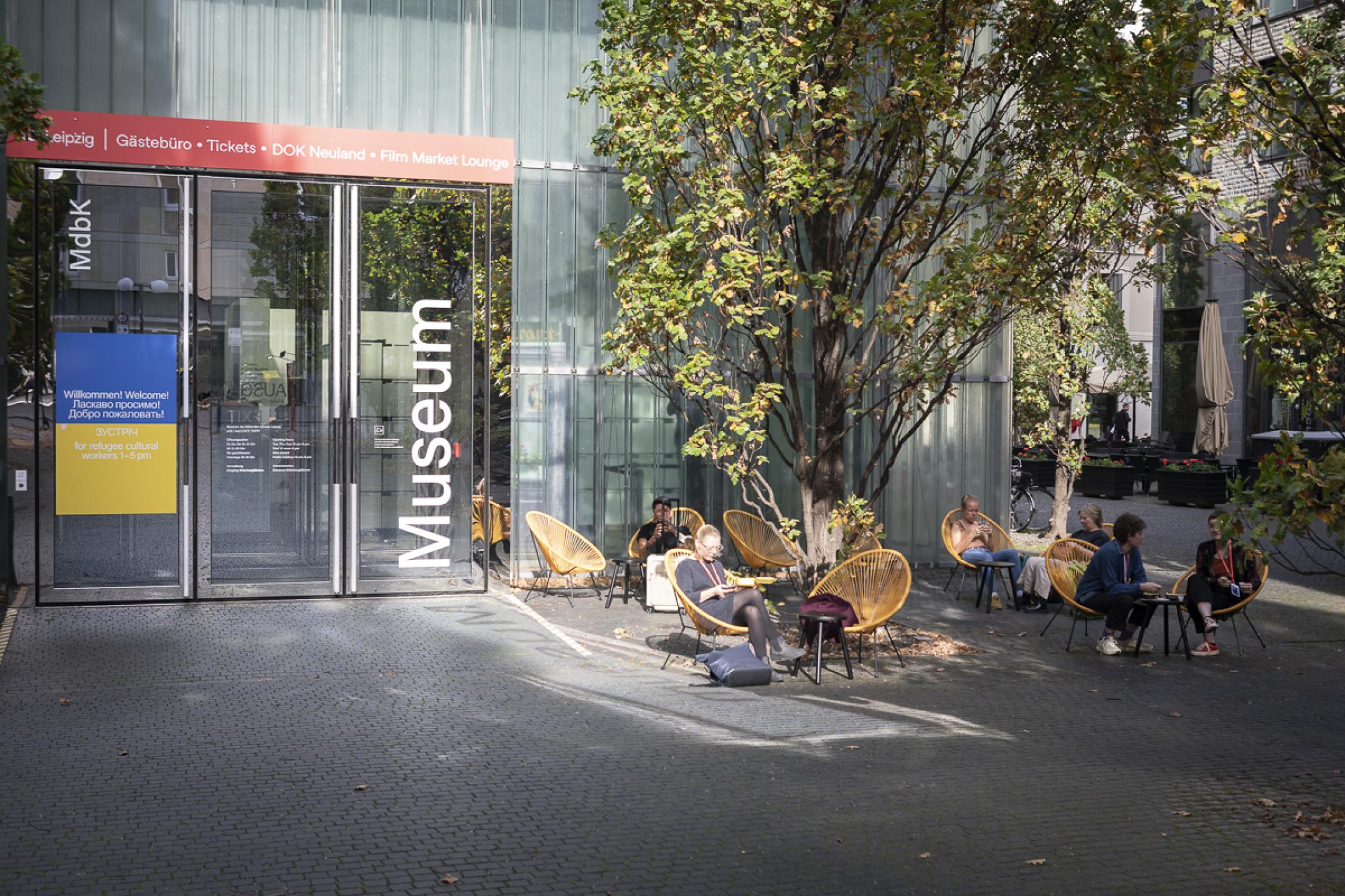 In front of the Festival Centre, people are sitting in cozy looking yellow chairs in the warm afternoon sun