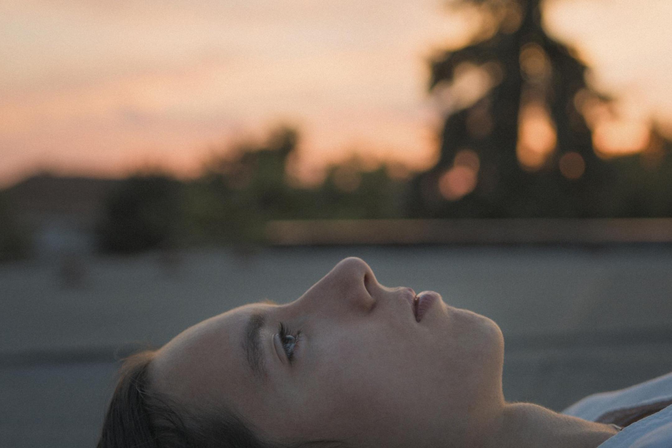 the side portrait of a young girl lying on the ground, the sky behind her is soft red