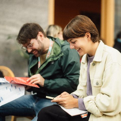 Zwei Personen sitzen auf nebeneinander und blättern im Festivalprogramm.