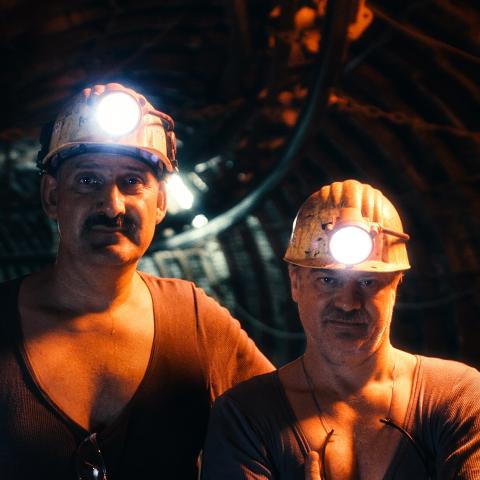 Ein Bild aus dem Film zeigt die Kumpel Locke und Langer, wie sie nebeneinander in der Mine stehen. Beide Männer haben ihre Helme auf und schauen in die Kamera.