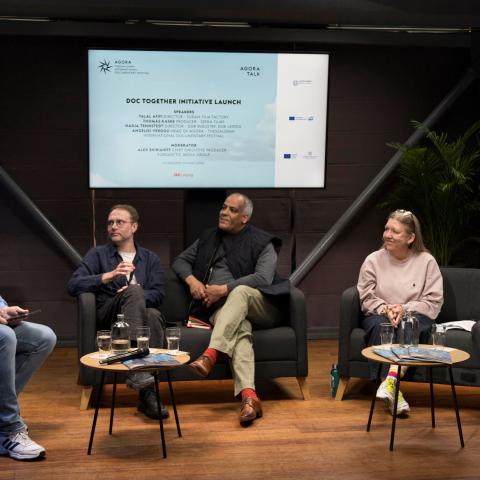 Three men and two women are sitting on a stage with a screen in the background displaying the topic "Doc Together Initiative Launch."