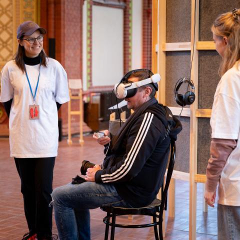 Zwei Volunteers unterstützen einen Besucher beim benutzen einer XR-Brille.