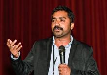 Picture of Selvamani Selvaraj on a stage talking with a microphone