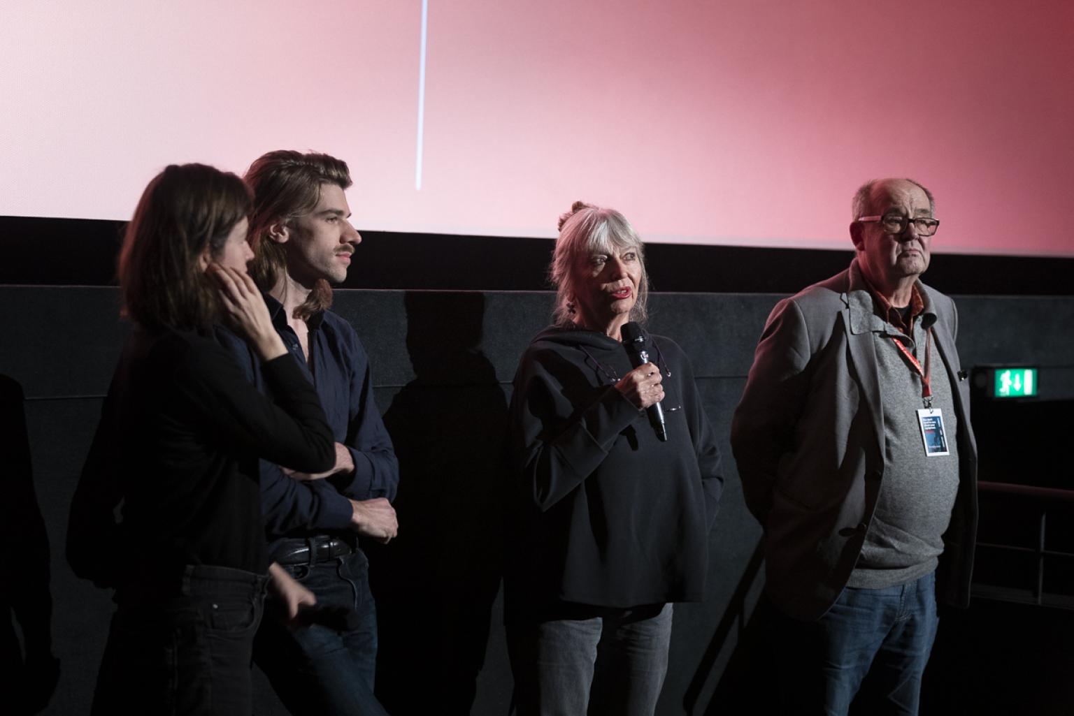 Vor der Leinwand stehen vier Personen: Thomas Plenert, Heike Misselwitz und die Kurator*innen der Retrospektive Carolin Weidner und Felix Mende