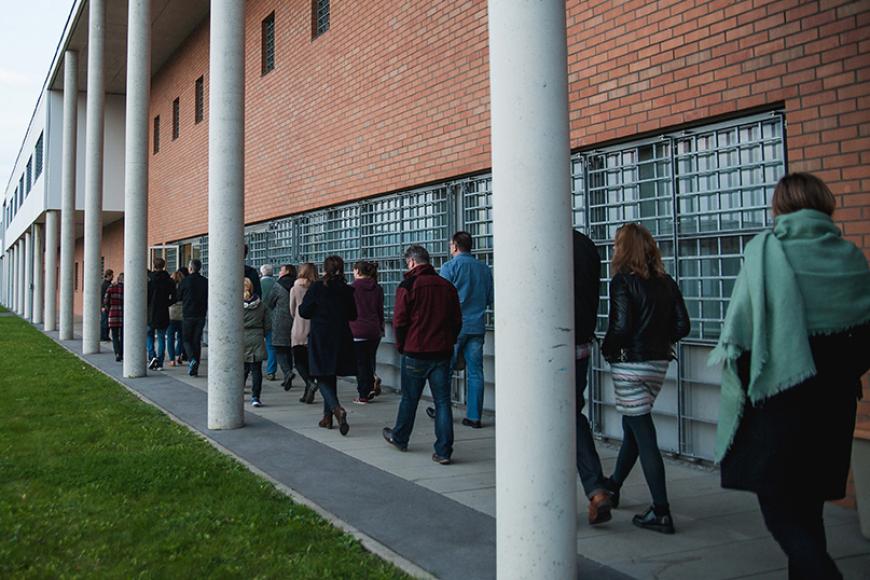 Mehrere Personen gehen an einem Gebäude mit vergitterten Fenstern entlang.