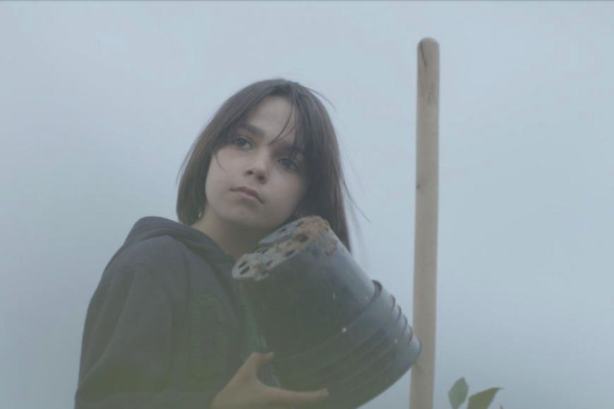 A child stands in the fog and holds a stack of plastic flower pots.