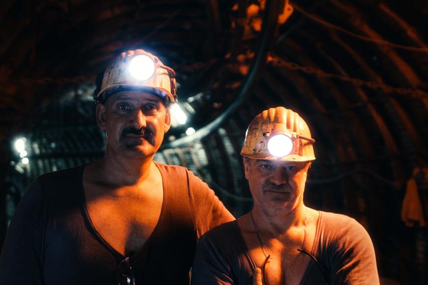 Ein Bild aus dem Film zeigt die Kumpel Locke und Langer, wie sie nebeneinander in der Mine stehen. Beide Männer haben ihre Helme auf und schauen in die Kamera.