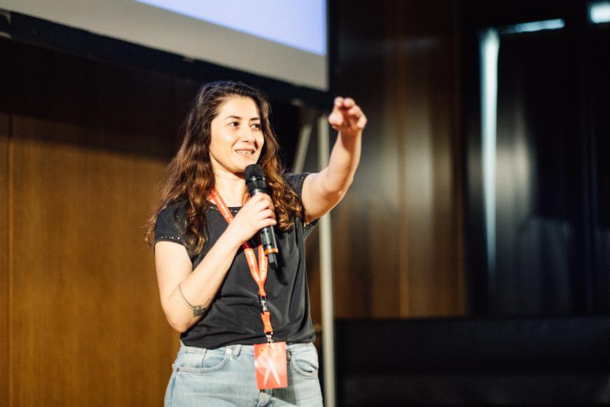 Guevara Namer on stage ist talking with a microphone